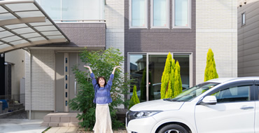 家と車の傍で両手をあげている女性の画像