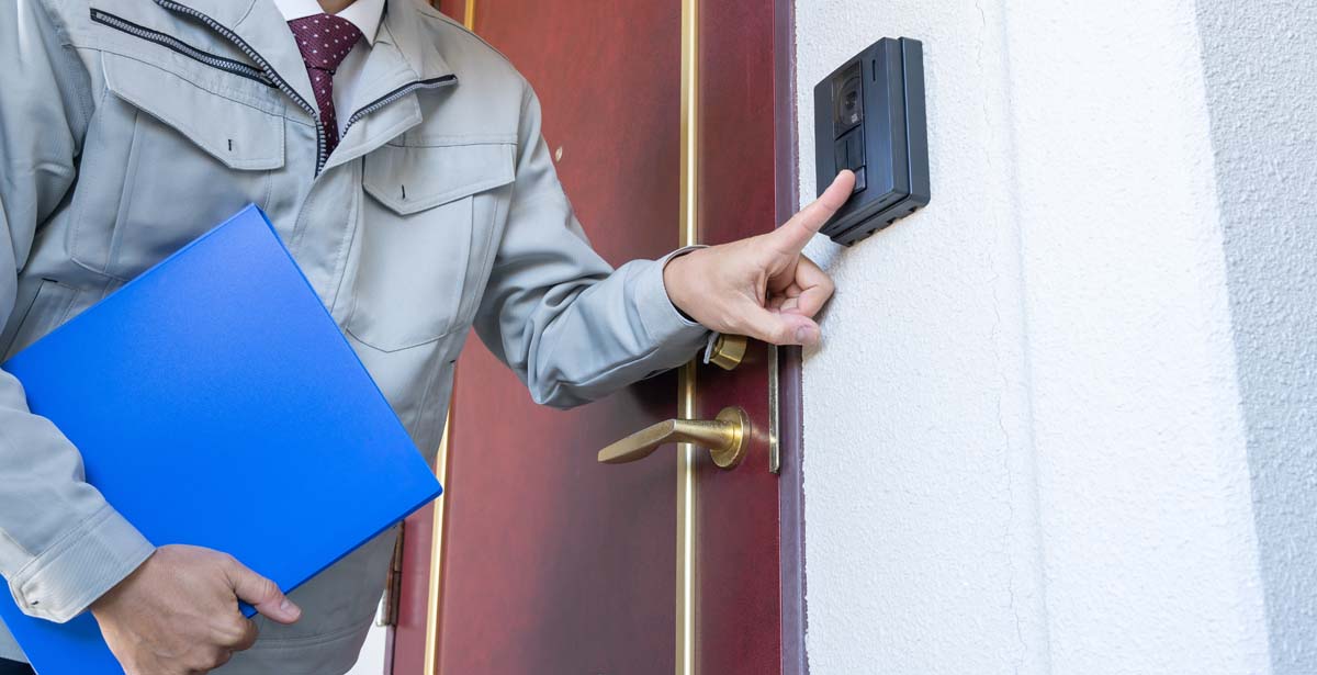 インターフォンを押す作業服の男性