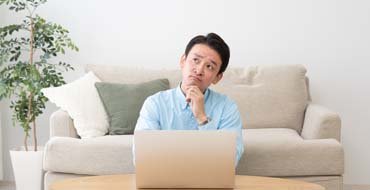 自宅でPCを見ながら考える男性