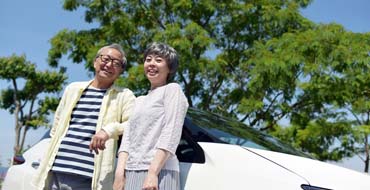 車の横に立つ笑顔のシニアカップル