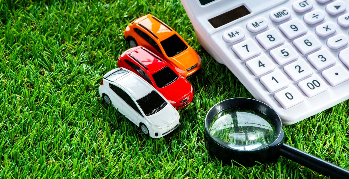 芝生に置かれた車の模型と電卓、虫眼鏡