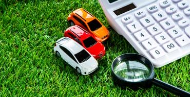 芝生に置かれた車の模型と電卓、虫眼鏡