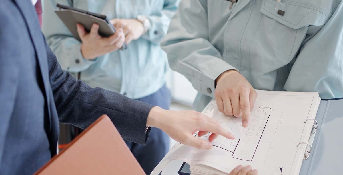 図面を見て打ち合わせをするスーツの男性と作業服の男性