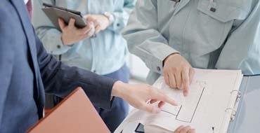 図面を見て打ち合わせをするスーツの男性と作業服の男性