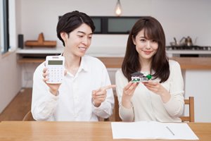 電卓を持った男性と家の模型を持った女性の画像